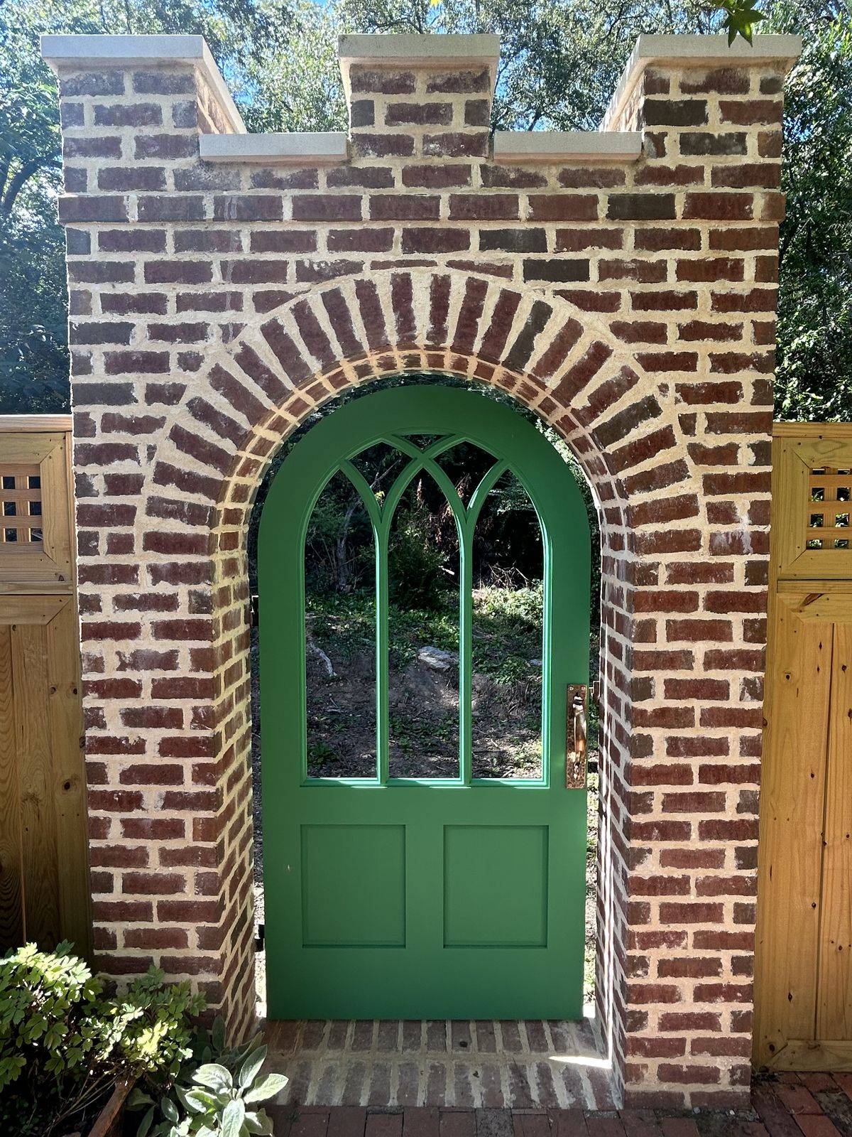 Custom green arched garden door set in a brick archway