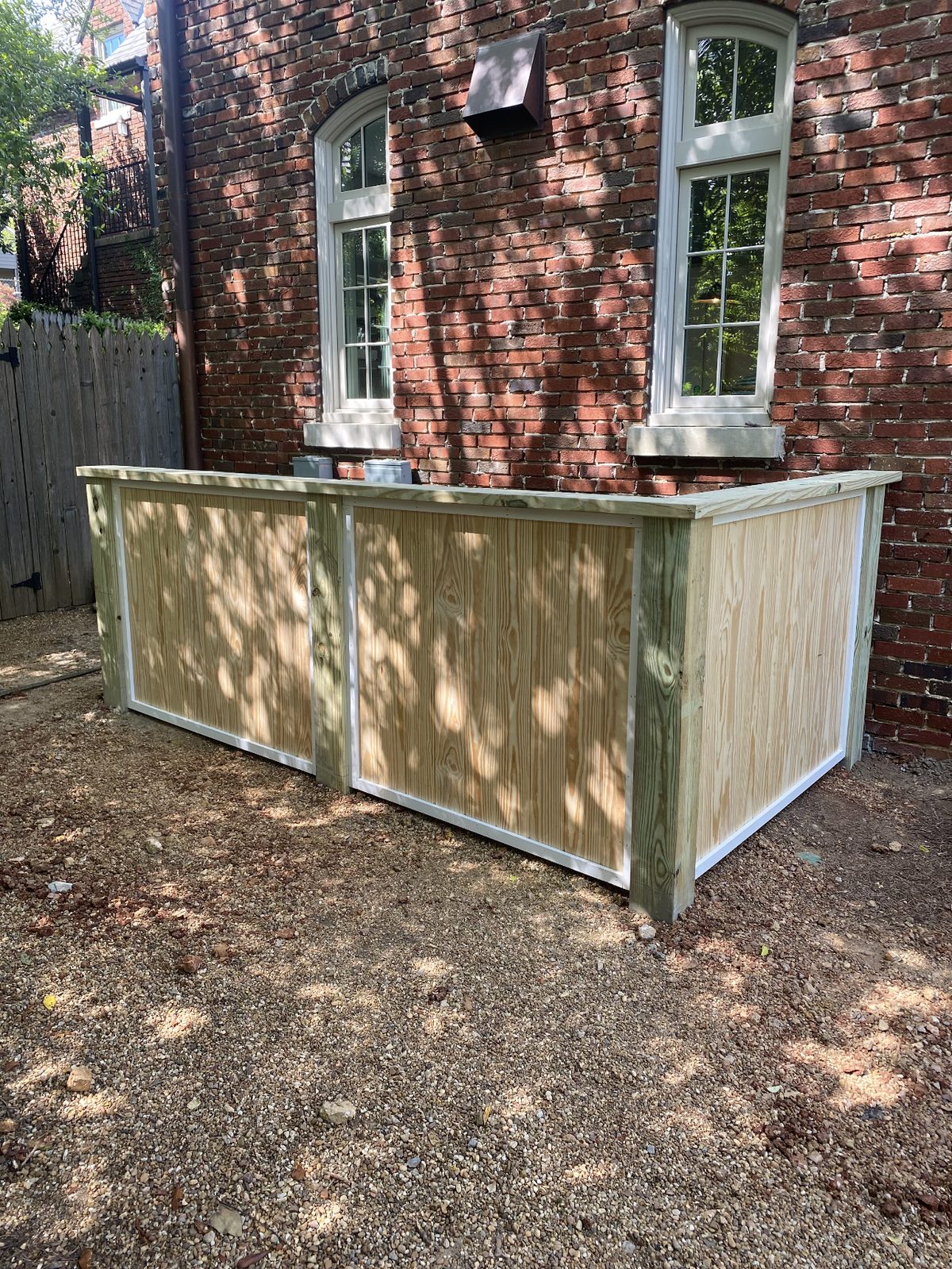 Pressure-treated wood enclosure with trim detail against a historic brick building